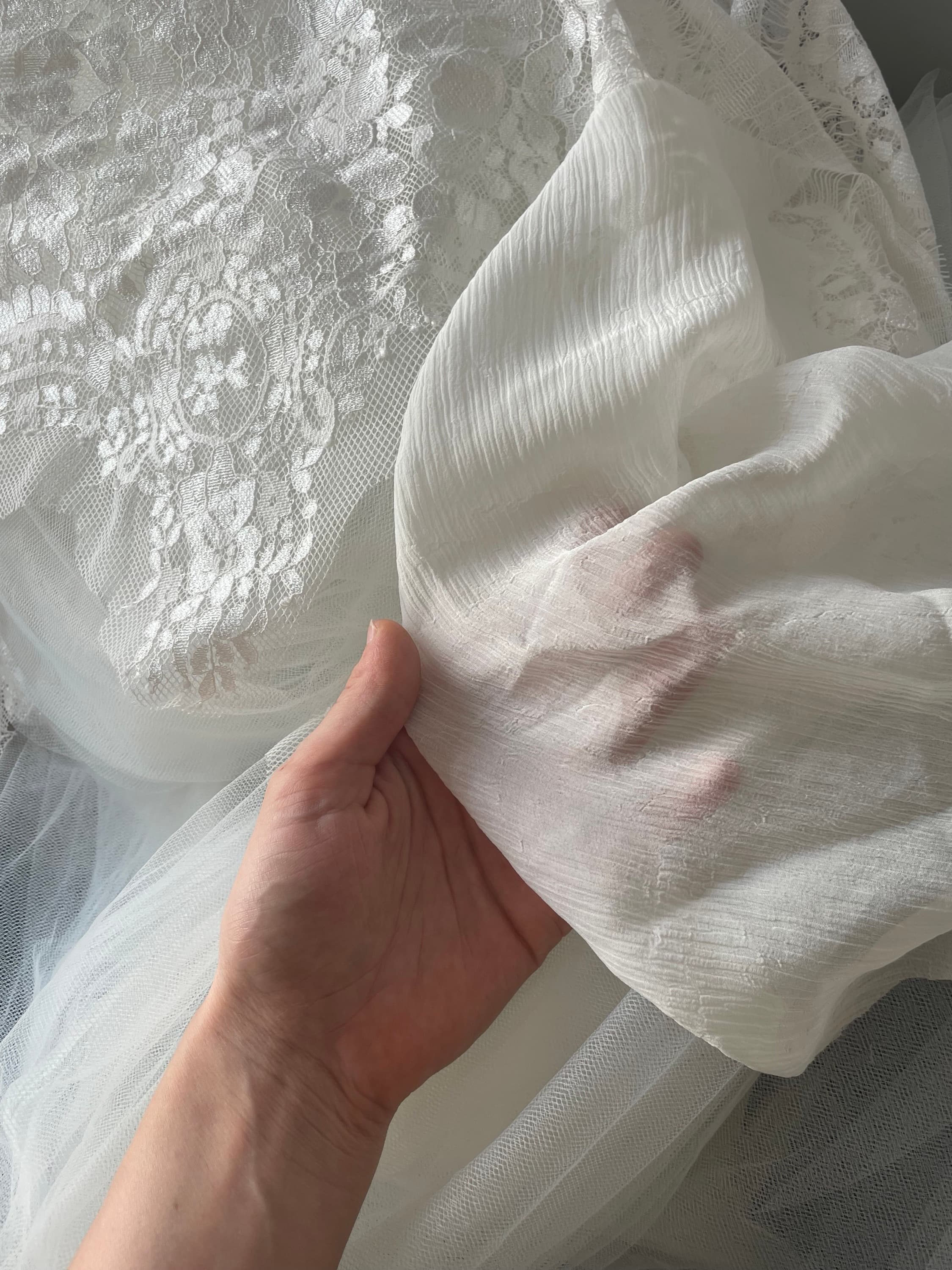 Une main soulevant un voile de crêpe au-dessus d'une dentelle et d'un tulle